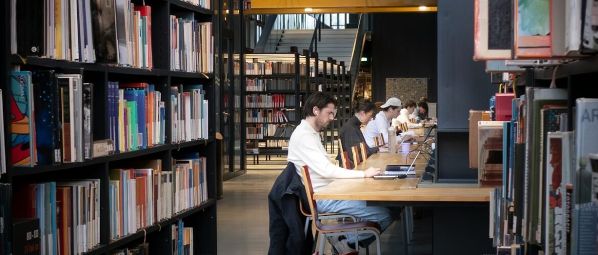 Personas estudiando con computadoras portátiles en mesas de una biblioteca.