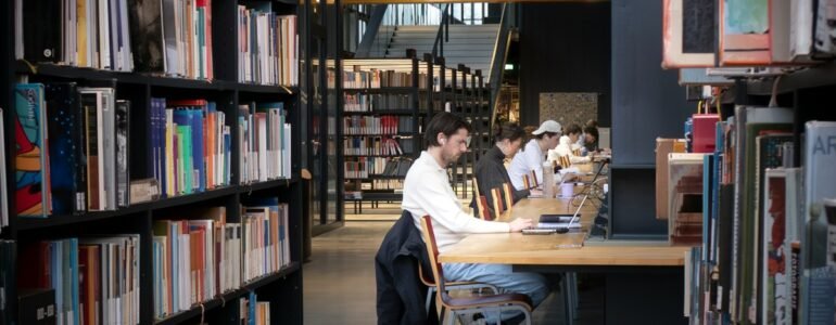 Personas estudiando con computadoras portátiles en mesas de una biblioteca.